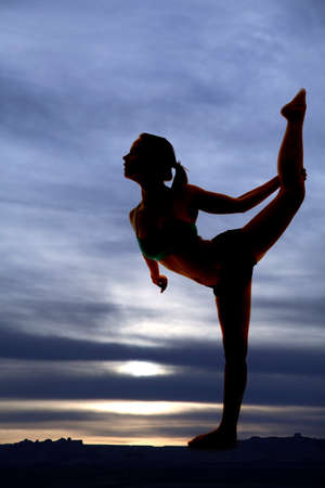 A silhouette of a woman stretching with her leg up.の写真素材
