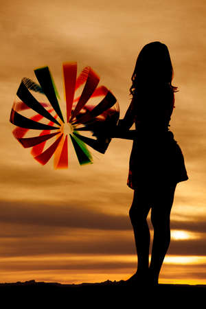 A silhouette of a woma holding on to a multi-colored beach ball.