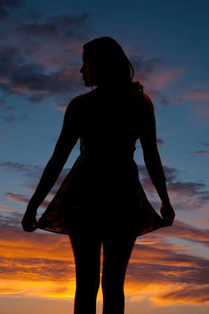 A silhouette of a woman playing with her dress looking to the side.の写真素材
