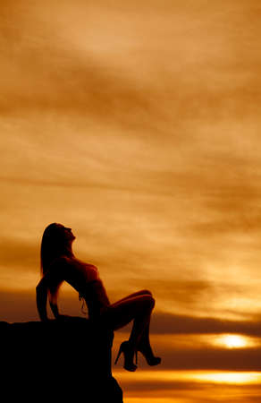 A silhouette of a woman sitting in a bikini in the sunset.の写真素材