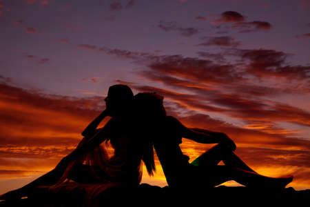A silhouette of two women sitting with their backs together.の写真素材