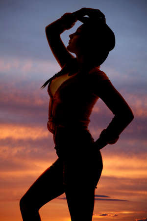 a silhouette of a woman holding on to her cowgirl hat.の写真素材