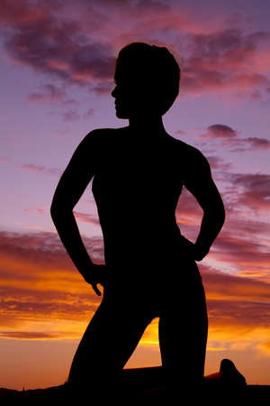 A silhouette of a woman kneeling with her hands on her hips.の写真素材