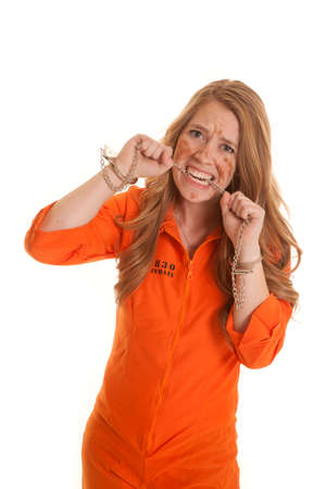 A woman in an orange jumpsuit in handcuffs biting a chain.の写真素材