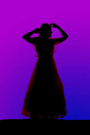 A silhouette of a woman in a dress with her hands by her head.の写真素材
