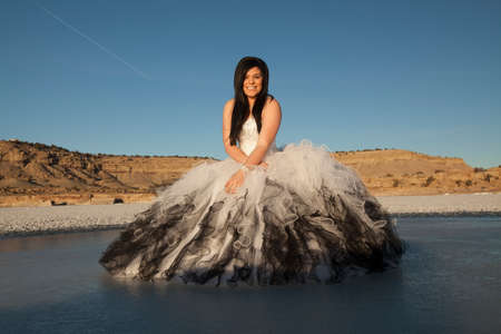 A woman in her formal dress with a smile on her face standing on a frozen lake in the outdoors.の写真素材