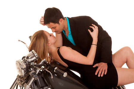 A couple laying back on her motorcycle getting ready to kiss.