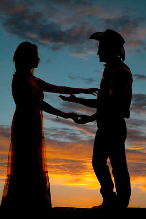 A silhouette of a cowboy reaching out and touching his beautiful woman.