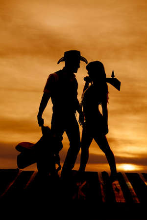 A silhouette of a cowboy holding his saddle and an Indian holding her club.の写真素材