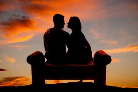 A silhouette of a couple sitting on a bench in the outdoors.の写真素材