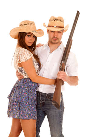 A a cowboy and cowgirl holding on to each other and he is holding on to a rifle.の写真素材