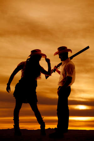 a silhouette of a cowgirl holding her hat while the cowboy is holding onto a gun.の写真素材