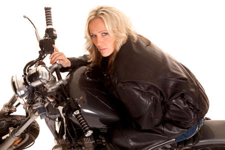 A woman in leather leaning on the gas tank of a motorcycle.の写真素材