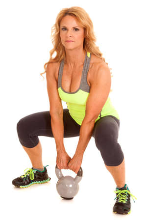 A woman in a green top with a kettle bell in a squat position.の写真素材