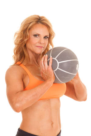 A mature woman in an orange sports bra holding a medicine ball.の写真素材