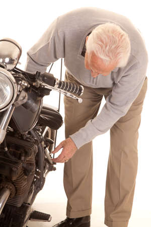 An old man with gray hair is bending over working on a motorcycle.の写真素材