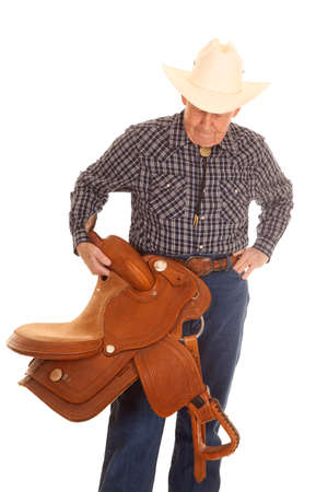 An old man standing holding a cowboy saddle.の写真素材