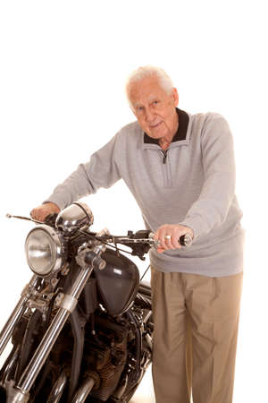 An old man standing by a motorcycle holding onto it.の写真素材