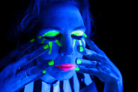 A woman is lit up with a black light and has her eyes closed.の写真素材