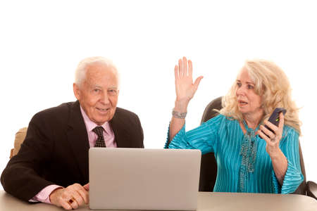 An older couple the man is working on a laptop while the woman is using a cell phone.の写真素材