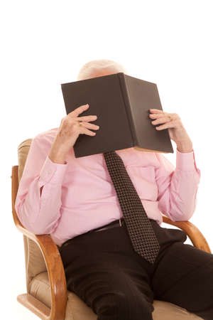 An older man sitting in his chair with a book up by his face studying.の写真素材