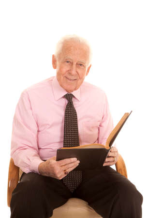 An elderly man  his pink shirt and tie with a smile on his face studying his book.の写真素材