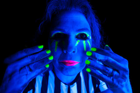 A woman has her hands by her face and glowing in the black light.の写真素材