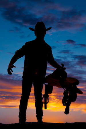 A silhouette of a cowboy holding a saddle in the sunset.の写真素材