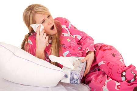 A woman in her pink pajamas with a tissue by her face.の写真素材