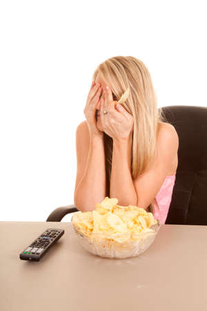 A woman covering her eyes watching t.v. and eating potato chips.の写真素材