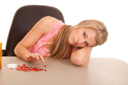 A woman laying on her arm with a pile of pills in front of her.の写真素材
