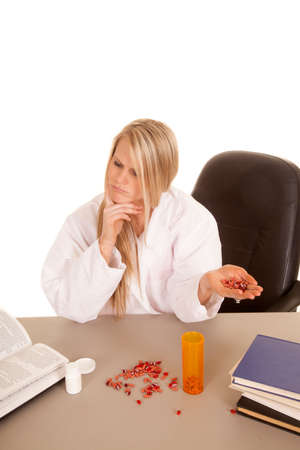 A woman pharmacist with pills in her hand, looking things up in a book.の写真素材