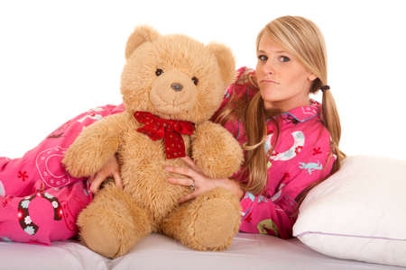 A woman laying on her side, holding on to her teddy bear with a pout on her face.の写真素材
