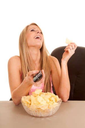 a woman holding on to a remote laughing, with a bowl full of chips in front of her.の写真素材