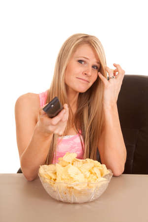 A woman holding on to a tv remote with a big bowl of chips in front of her.の写真素材