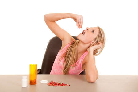 A woman with pills on the table, getting ready to take one.の写真素材