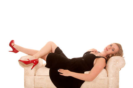 A woman laying back on her couch in her black dress and red shoes.の写真素材