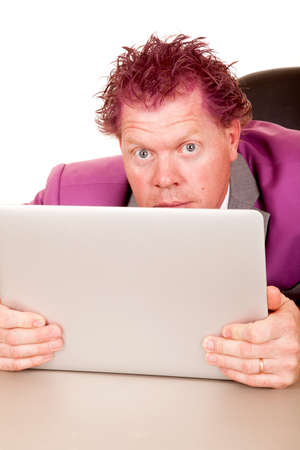 A man in his purple suit looking over the top of his computer with a funny expression.の写真素材