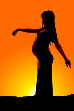 a silhouette of a woman who is pregnant standing outdoors.の写真素材