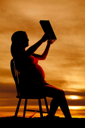 a silhouette of a woman holding and reading a book.の写真素材