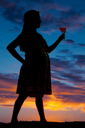 A silhouette of a woman standing holding a drink in her hand.の写真素材