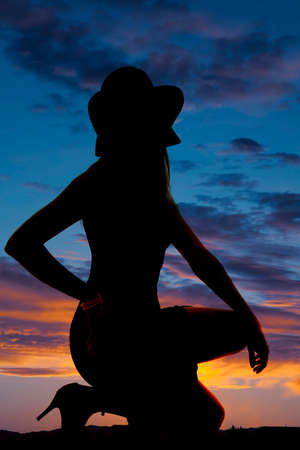 A silhouette of a woman kneeling on the ground wearing a hat.の写真素材