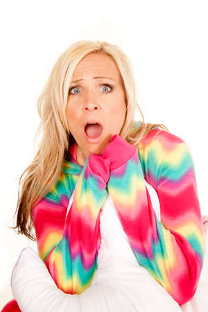 a woman in her colorful pajamas holding on to her pillow with a shocked expression on her face.の写真素材