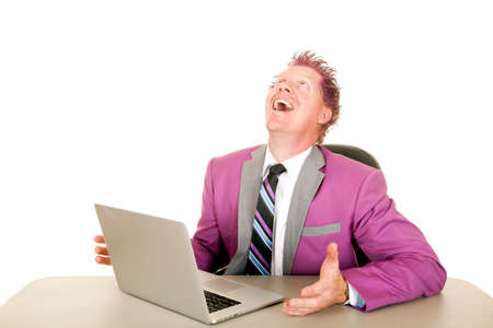 A man in a purple suit looking up laughing while on his computer.の写真素材