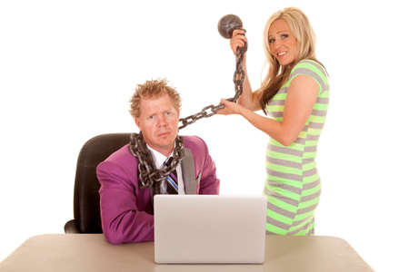 A business man with a sad expression on his face while his woman co-worker is holding on to his ball and chain.の写真素材