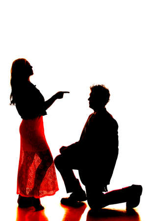 a silhouette of a man and woman, the man is kneeling and the woman is showing attitude.の写真素材