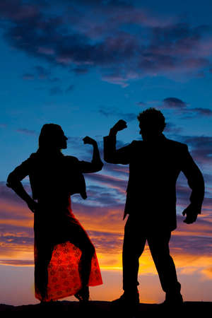 A silhouette of a man and woman looking at each other flexing their muscles.の写真素材