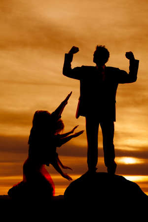 A silhouette of a woman on her knees bowing to the man flexing.の写真素材