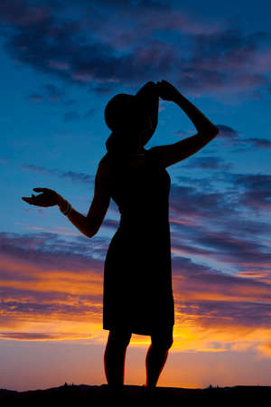 a silhouette of a woman standing touching her hat in the outdoors.の写真素材