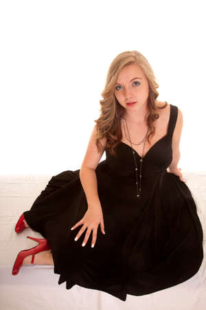 a woman sitting in her black dress with her red shoes showing.の写真素材